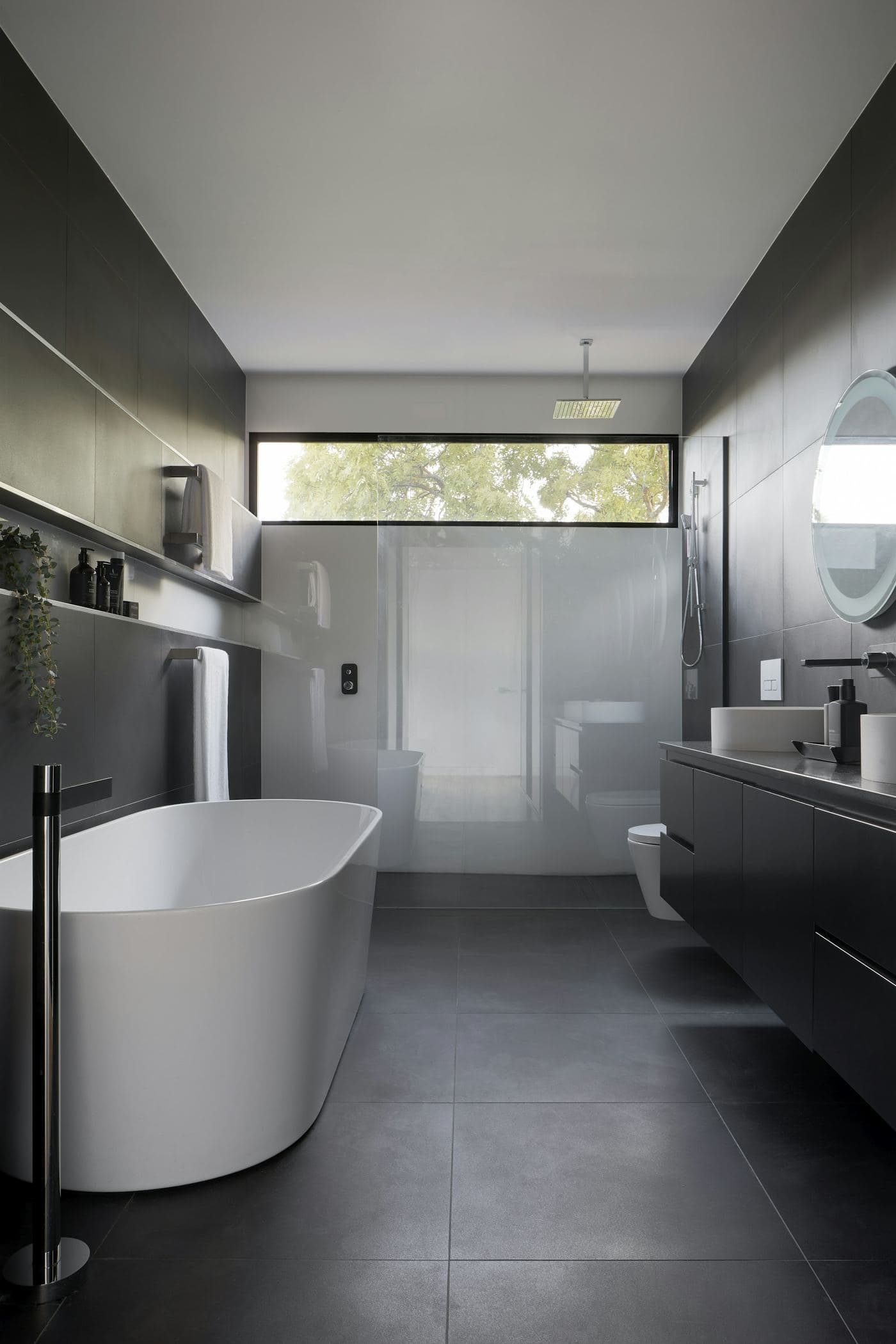 Dark-toned bathroom with a white freestanding bath lit from a high skylight