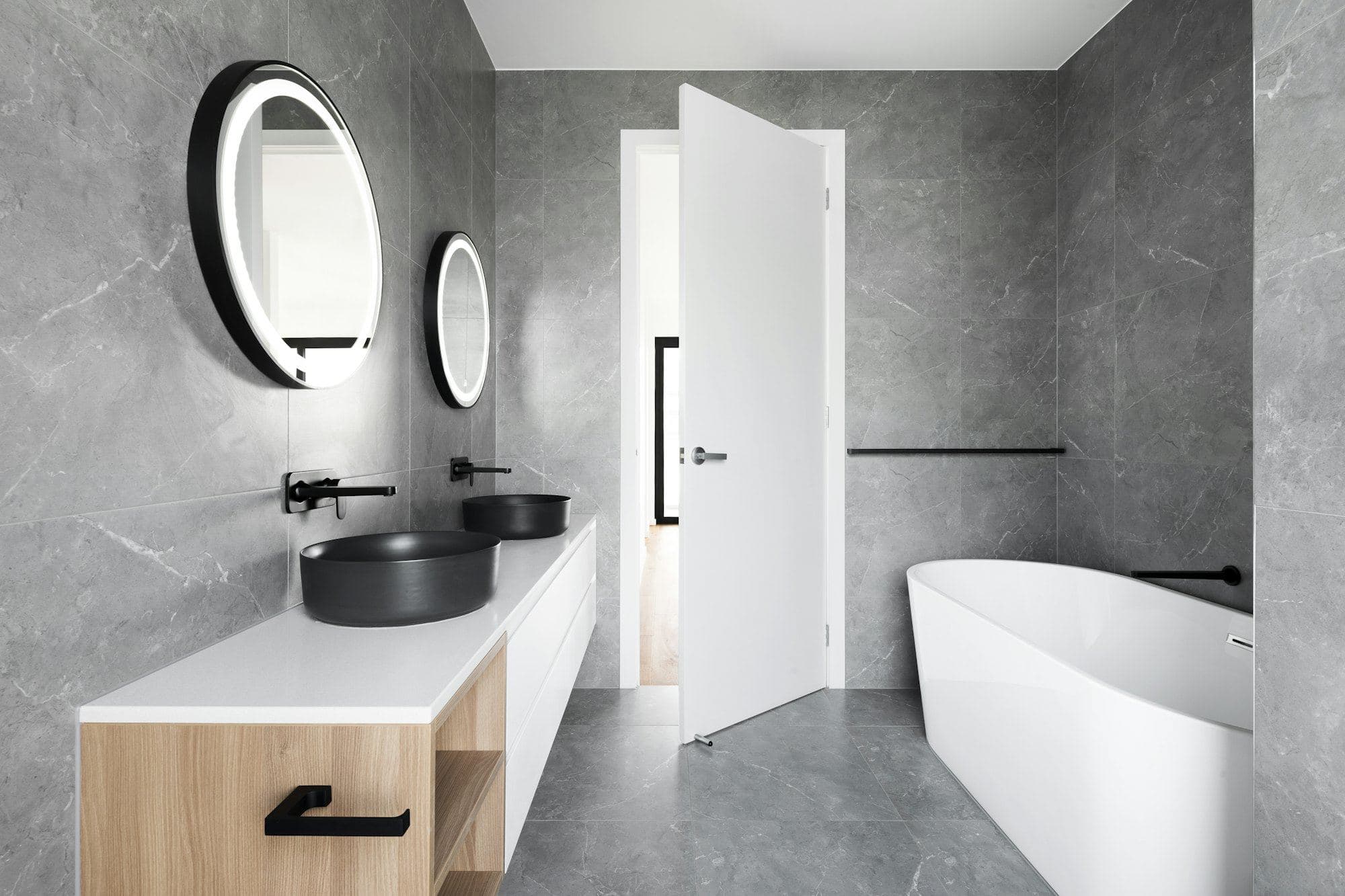 Bathroom with grey stone walls, a black basin on a timber vanity and a round black-framed mirror