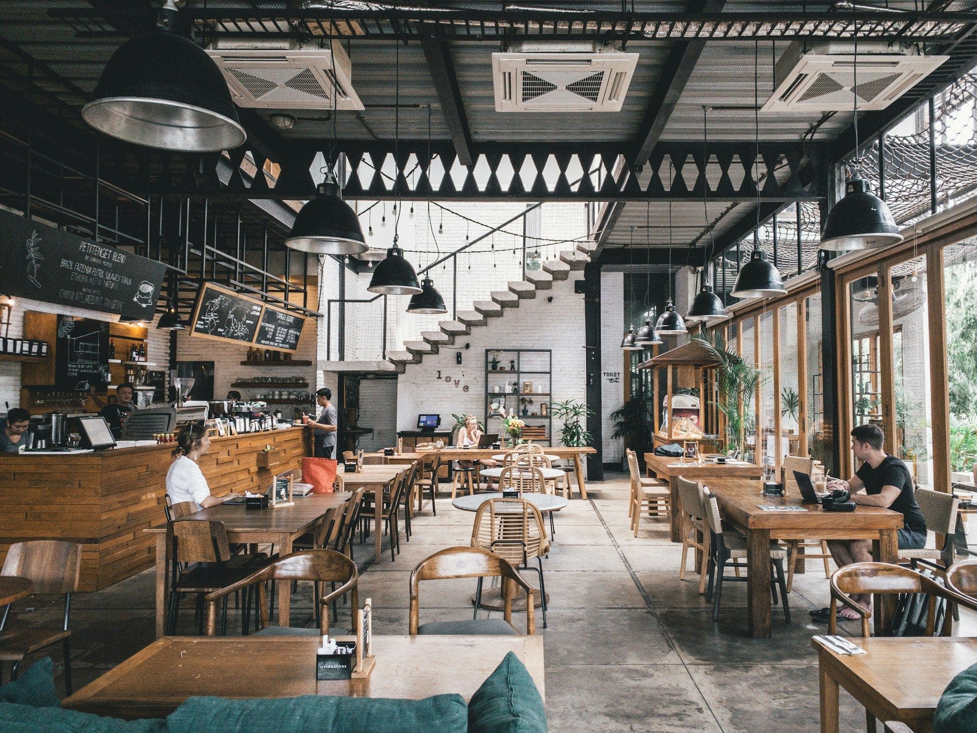 ร้านกาแฟในโกดังเก่า เพดานโครงเหล็ก โคมไฟห้อย และโต๊ะไม้ยาว
