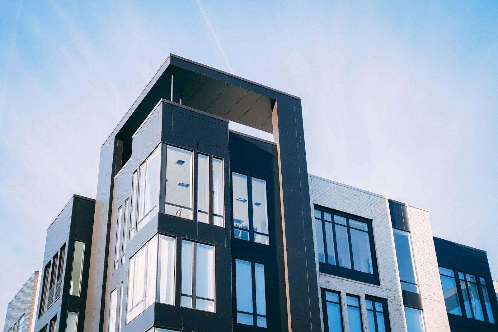 Looking up at a black-and-white apartment building with crisp window frames against a blue sky