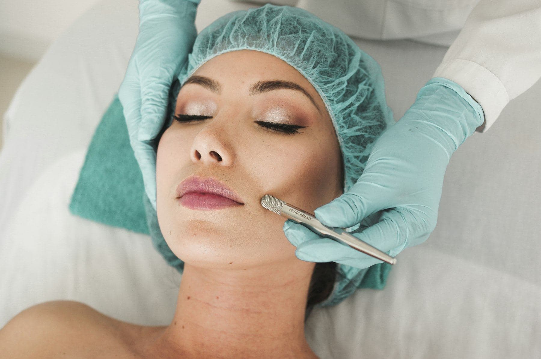 A gloved practitioner treating the face of a client lying with eyes closed