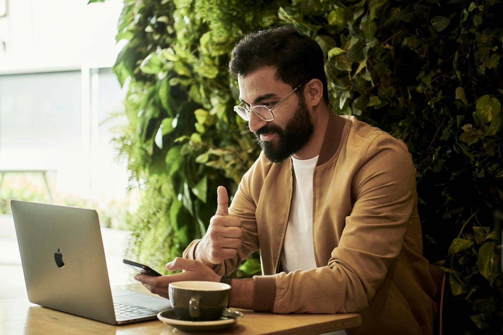 A man working on a laptop and phone in a café with plants