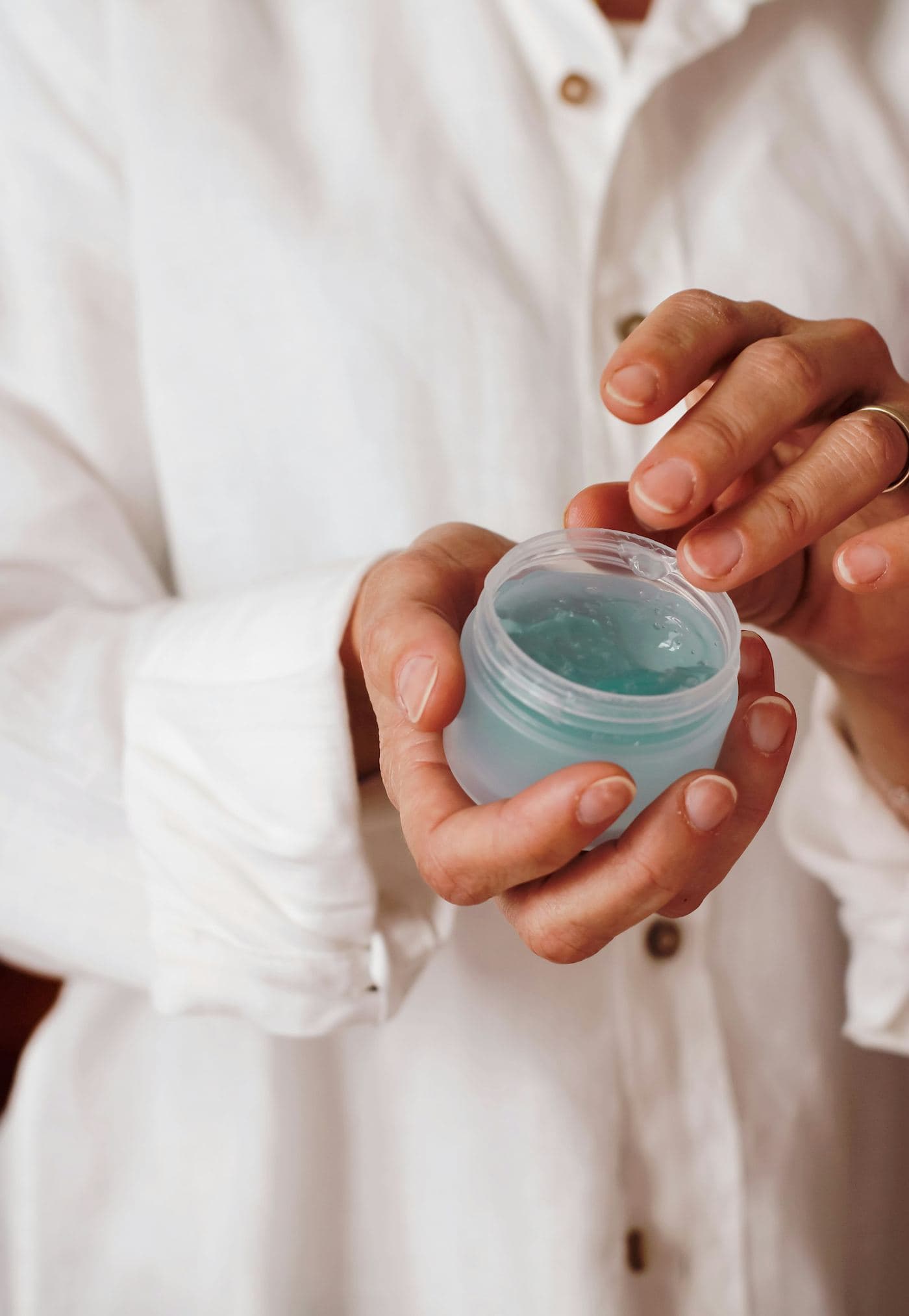 Two hands holding a small jar of clear blue gel against a white shirt