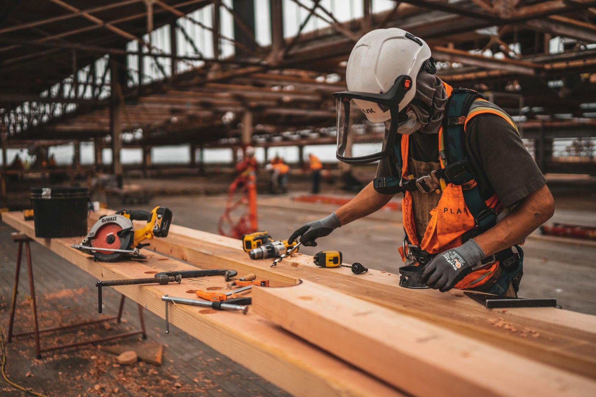 Carpenter in a hard hat measuring and cutting timber on a workshop bench
