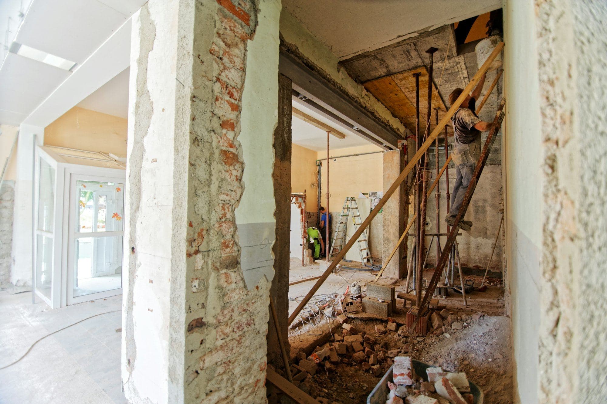 A site mid-demolition with exposed brick, timber props and a worker on a ladder