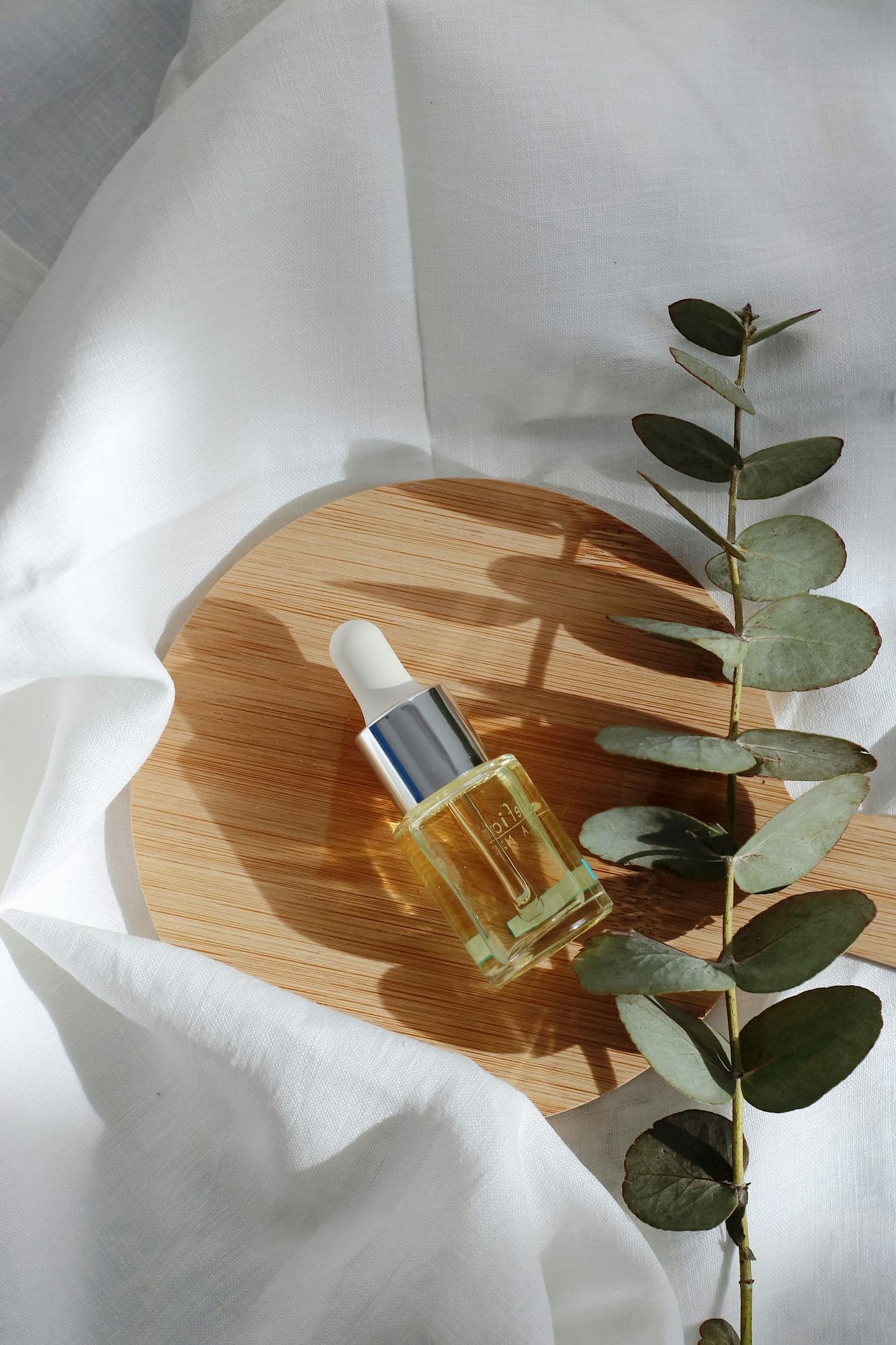 A small amber serum bottle on a wooden board beside a eucalyptus sprig