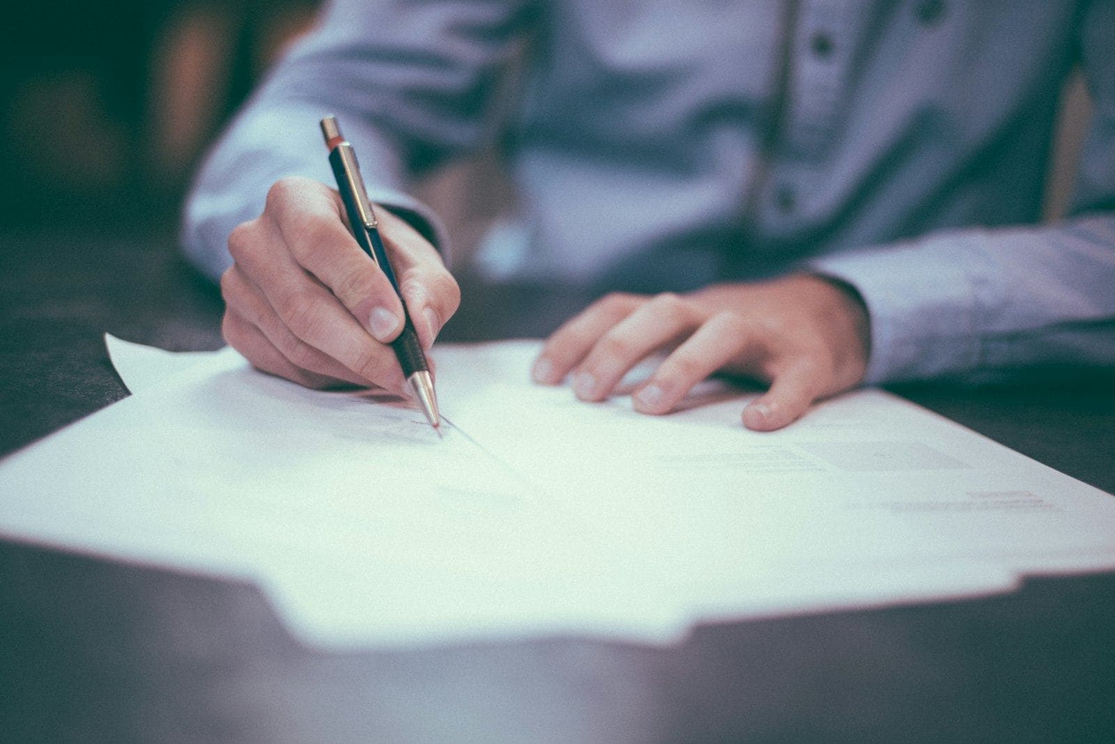 A hand signing a document on a desk