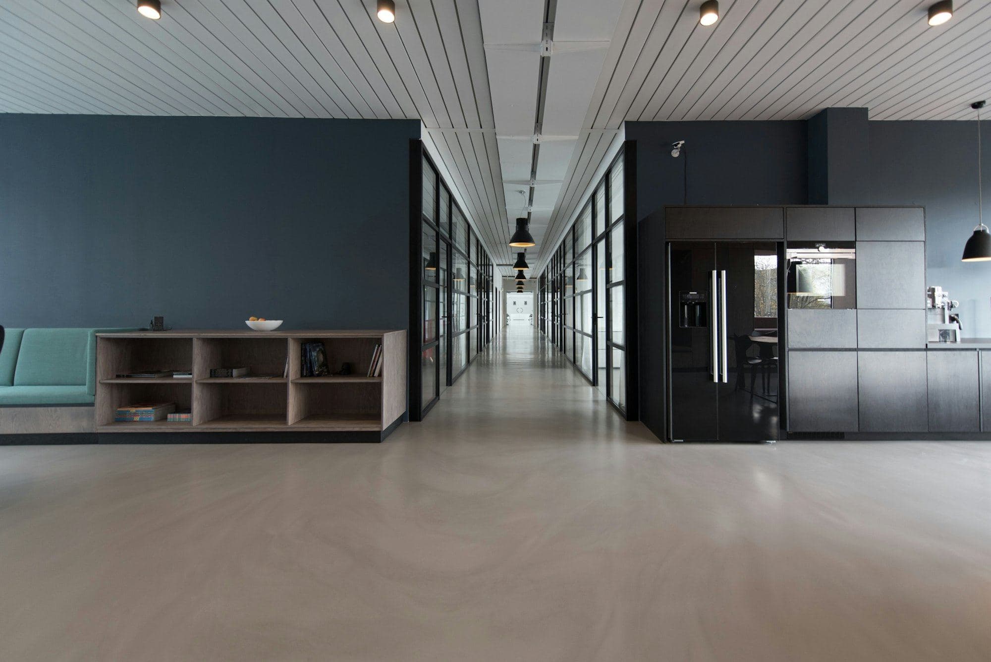 Office corridor with a dark grey wall, timber shelving and a row of glass rooms