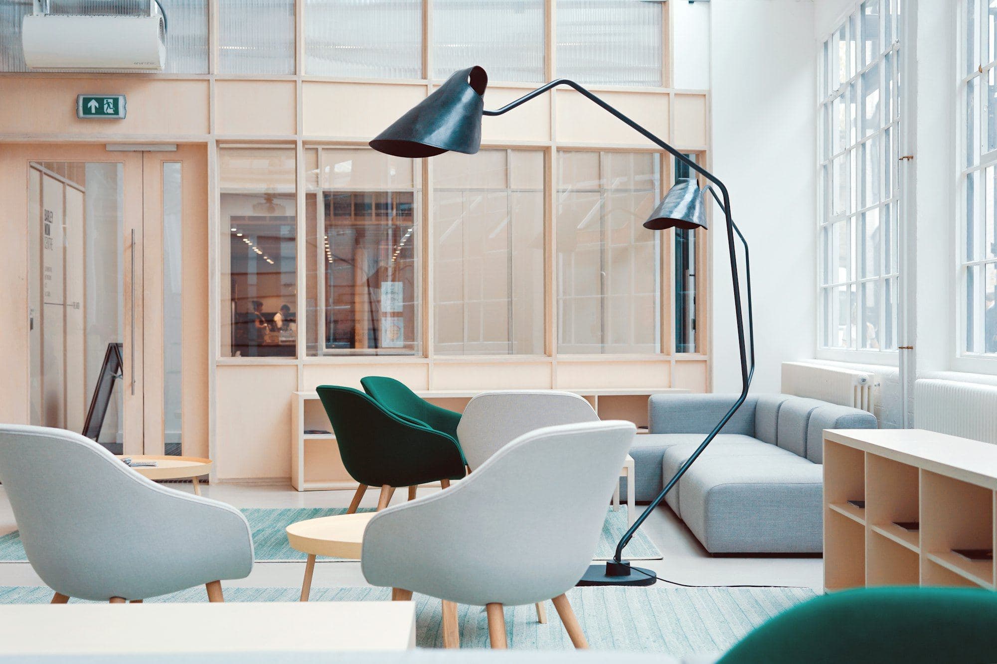 Office lounge corner with pale upholstered chairs, a black floor lamp and timber-framed glazing